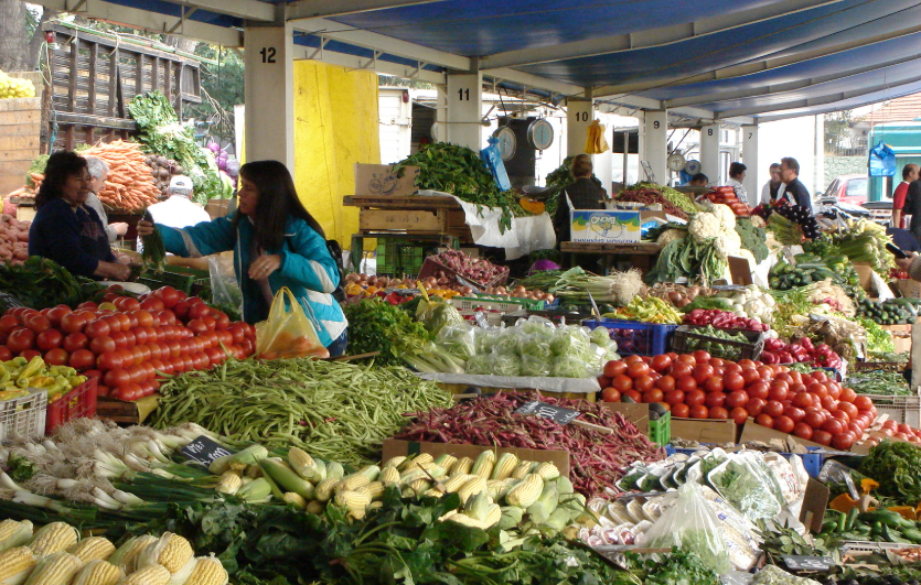 Cajones con verduras frescas bajo toldos azules de una feria